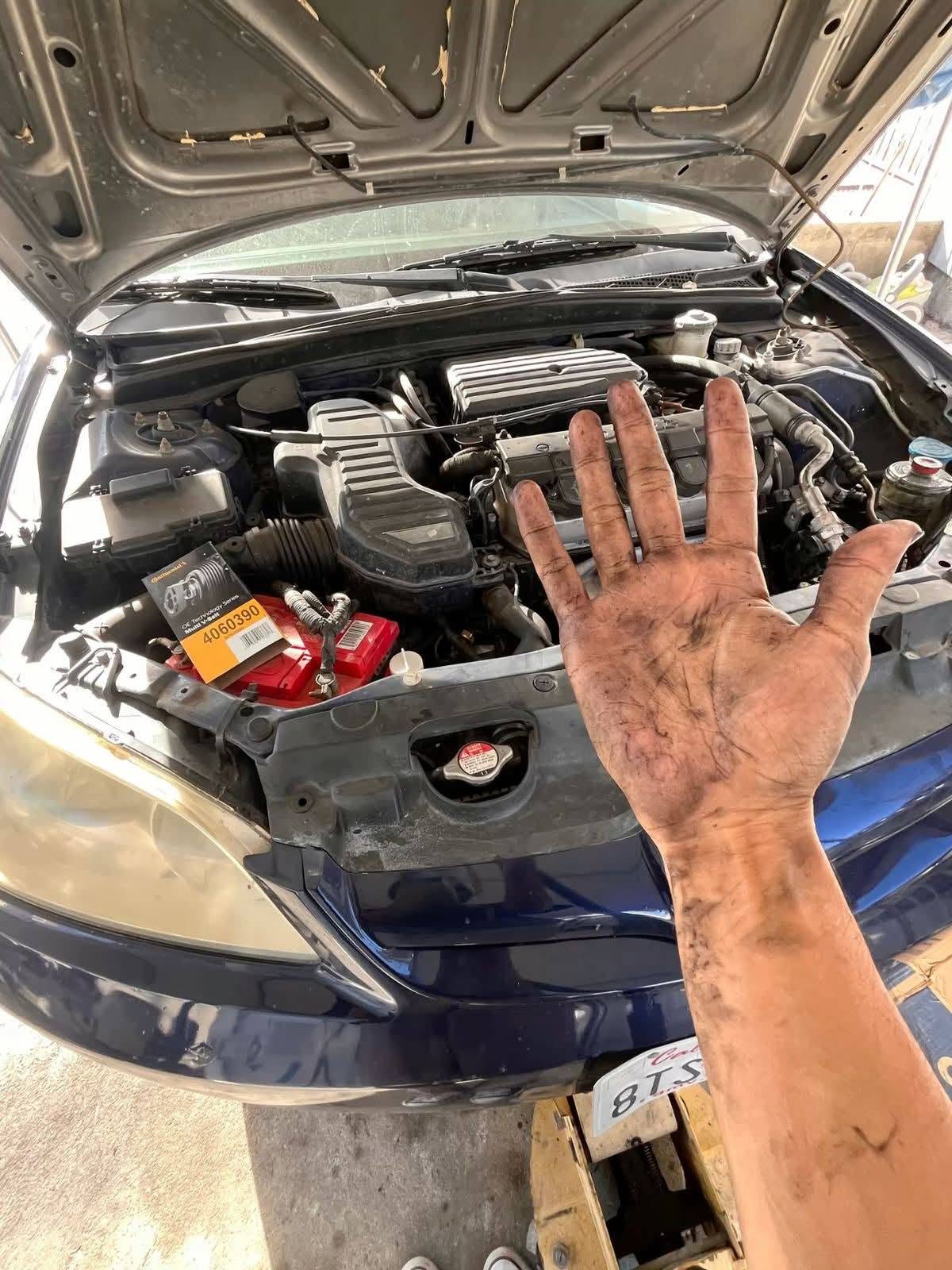 Mobile mechanic's hand above an engine bay during a repair with a replacement belt on the battery